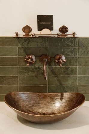 Un baño con un lavabo cobrizo, paredes de azulejos verdes y tres grifos de cobre.