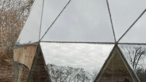 Une structure moderne en verre aux lignes géométriques, dotée d’une surface réfléchissante, et entourée d’un espace de détente extérieur.