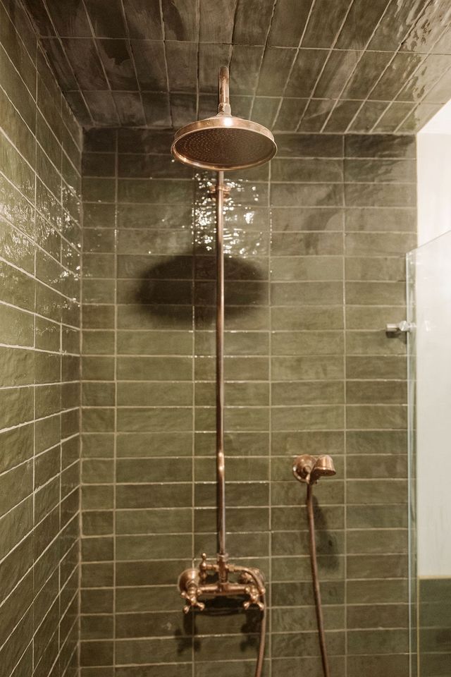 A shower with a copper fixture, a tiled wall, and a visible shadow.