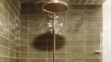 A shower with a copper fixture, a tiled wall, and a visible shadow.
