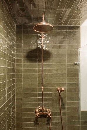 Ducha con grifería de cobre, pared con azulejos y una sombra visible.
