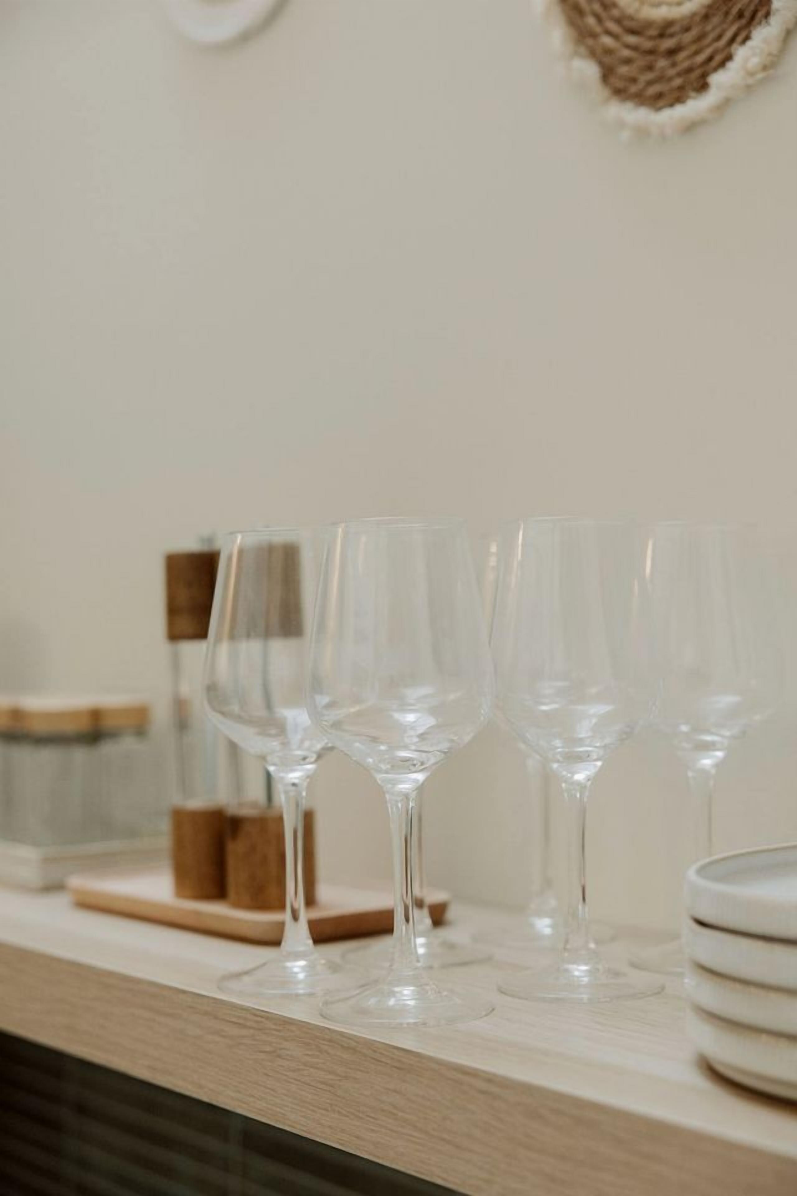 A kitchen counter with clear glass wine glasses, a stack of white plates, and a wooden cutting board.