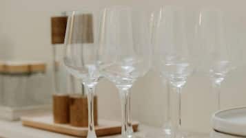 A kitchen counter with clear glass wine glasses, a stack of white plates, and a wooden cutting board.