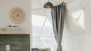 Une pièce aménagée comme une tente, avec un banc en bois, une table blanche et une suspension lumineuse.