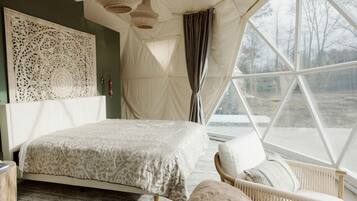 A bedroom with a bed, a chair, a large window, and a decorative wall piece.