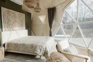 Ein Schlafzimmer mit einem Bett, einem Sessel, einem großen Fenster und einer Wanddekoration.