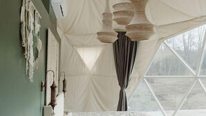 Une pièce aménagée comme une tente, avec un lit, des lampes suspendues et une vue par la fenêtre.