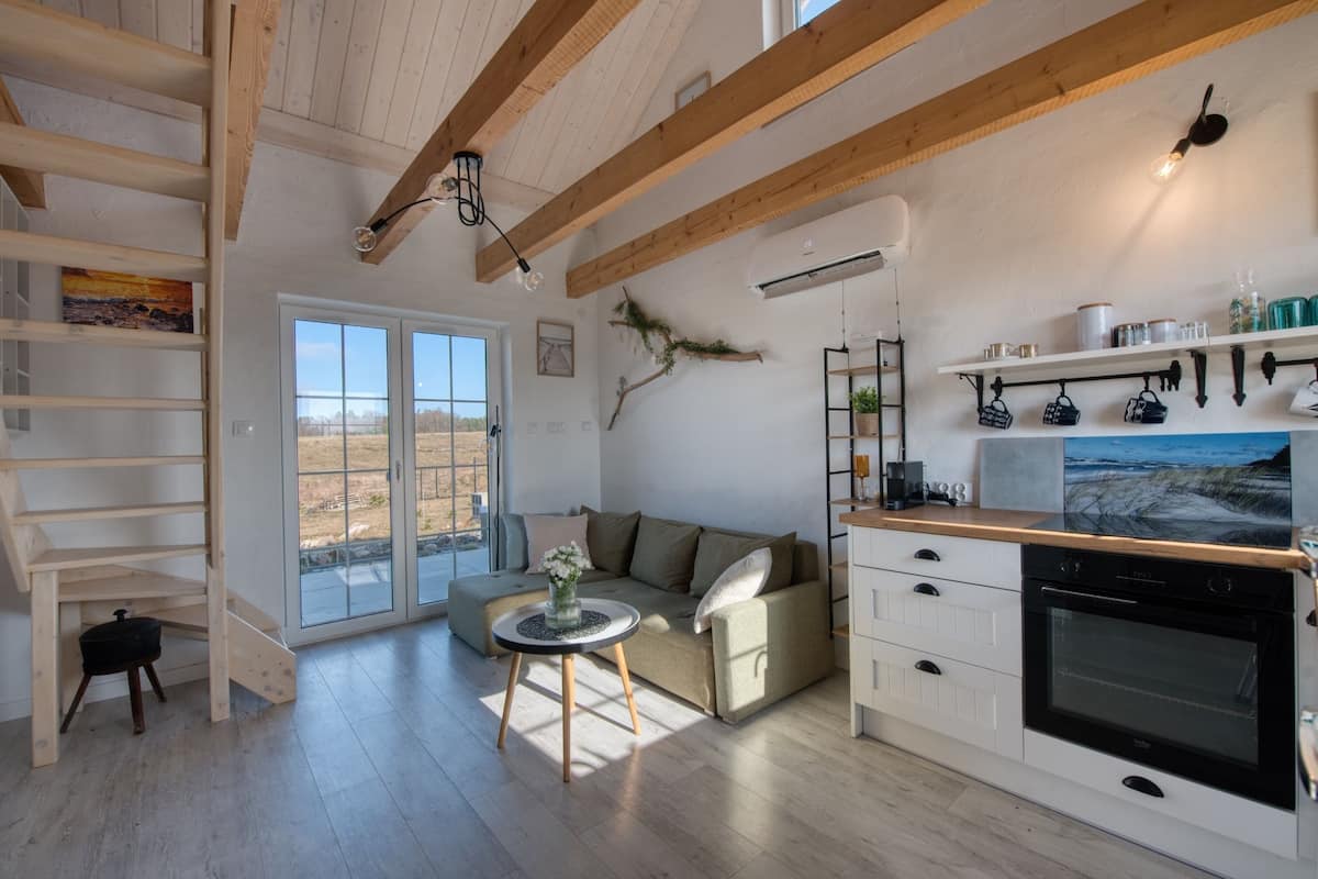 Une cuisine moderne dotée d’un four encastré, un coin repas avec une table ronde et un escalier menant à une mezzanine.