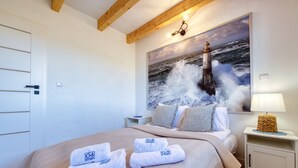 A bedroom with a bed, a painting of a lighthouse, a nightstand, and a lamp.