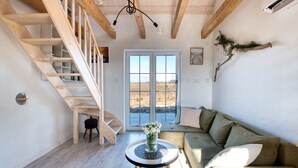 A room with a wooden staircase, a sofa, a round table with a vase, and a large window with a view.