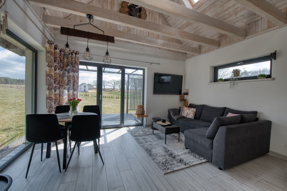 Un salon moderne avec un canapé gris, des fauteuils noirs, une table basse et un téléviseur fixé au mur.