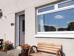 A building with a white exterior, a wooden bench, and a window with a white frame. - Taigh Ban (Nairn)