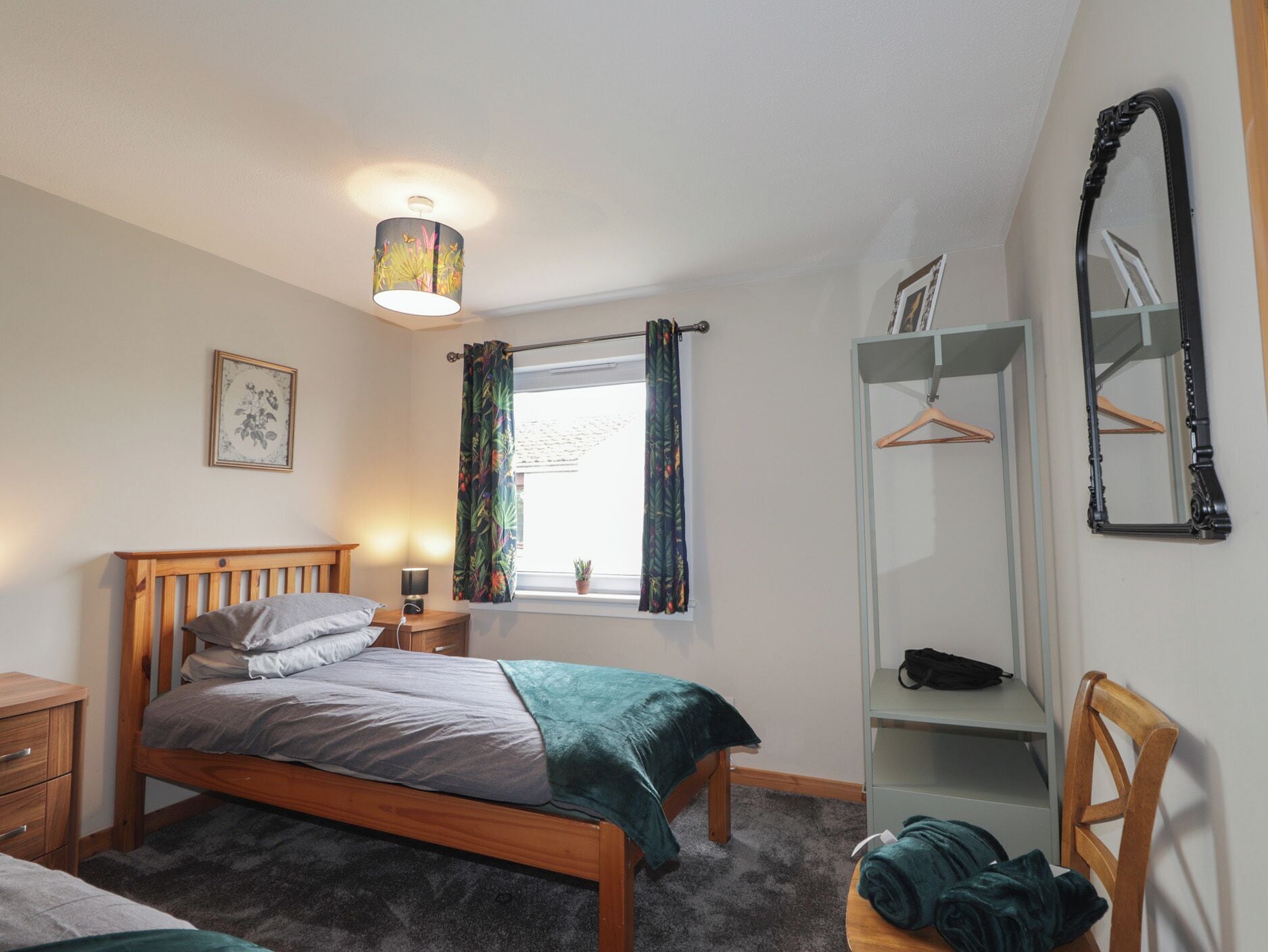 A bedroom with a bed, a bedside table, a lamp, a window with curtains, a wardrobe, and a mirror.