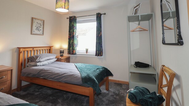 Une chambre à coucher comprenant un lit, une table de chevet, une lampe, une fenêtre avec des rideaux, une armoire et un miroir.