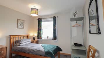 A bedroom with a bed, a bedside table, a lamp, a window with curtains, a wardrobe, and a mirror.