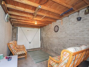 A room with a wooden ceiling, a dartboard, a white garage door, wicker furniture, and a brick wall. - Taigh Ban (Nairn)