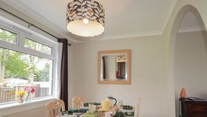 Un coin repas avec une table ronde, des chaises, un luminaire suspendu, une fenêtre avec des rideaux et un miroir au mur.