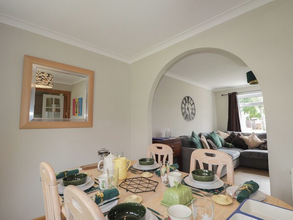 A dining area with a table set for four, a mirror on the wall, and a sofa in the background. - Taigh Ban (Nairn)