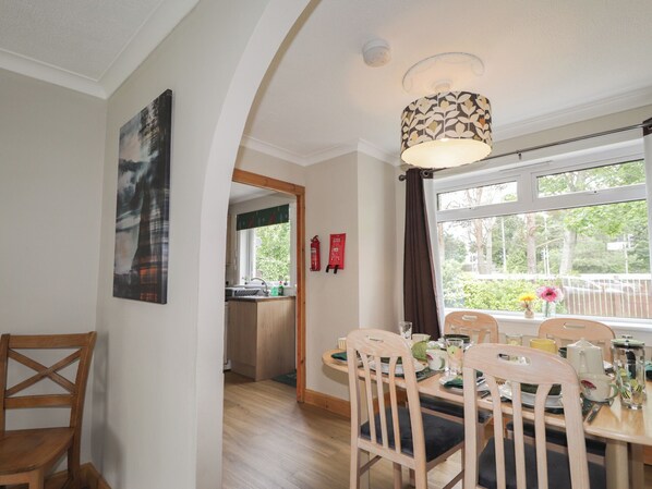 A dining area with a table set for four, wooden chairs, a pendant light fixture, and a view of the outdoors through a window. - Taigh Ban (Nairn)