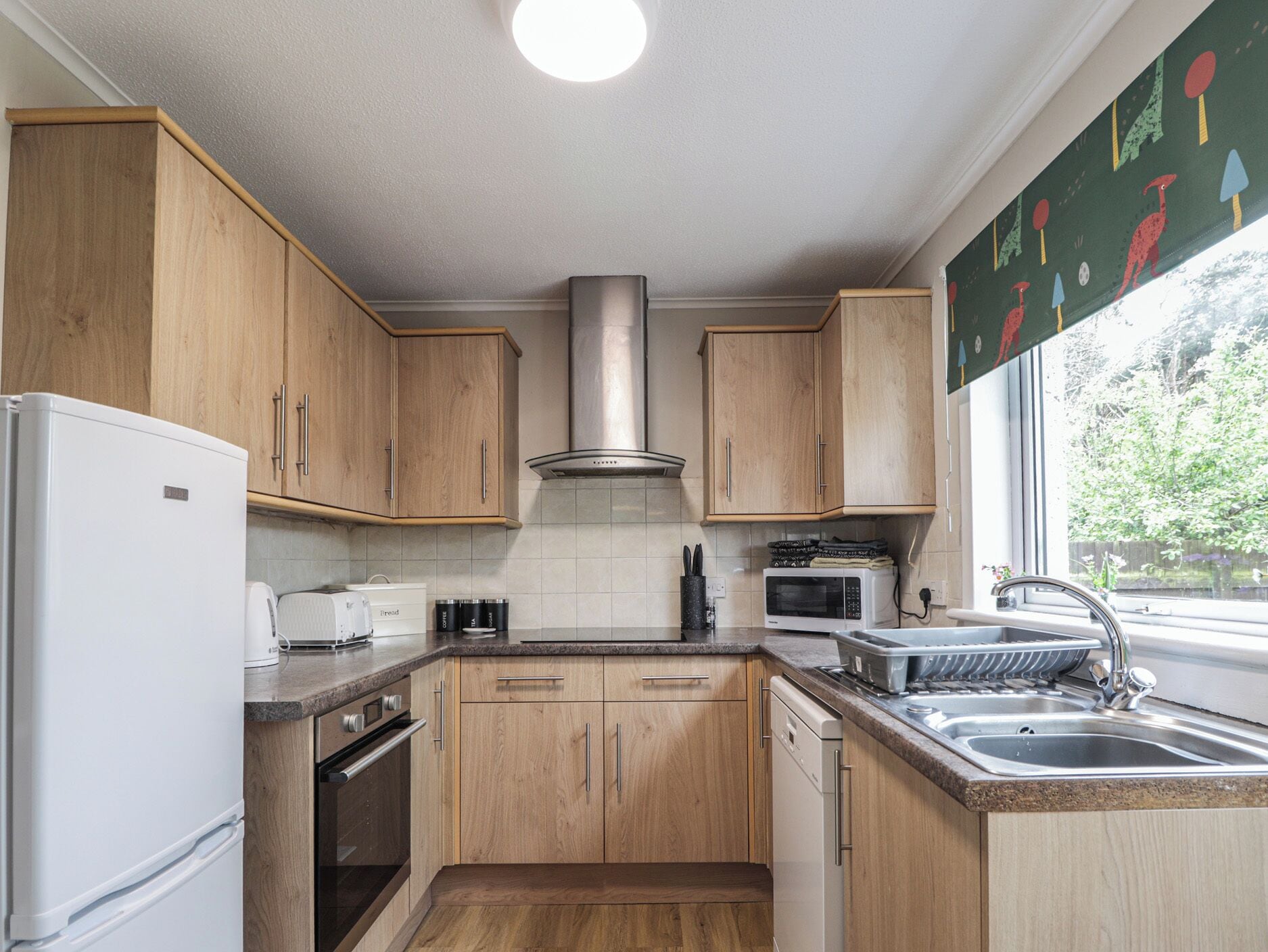 A kitchen with wooden cabinets, a stainless steel range hood, a microwave, a dishwasher, and a sink.