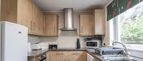 A kitchen with wooden cabinets, a stainless steel range hood, a microwave, a dishwasher, and a sink.