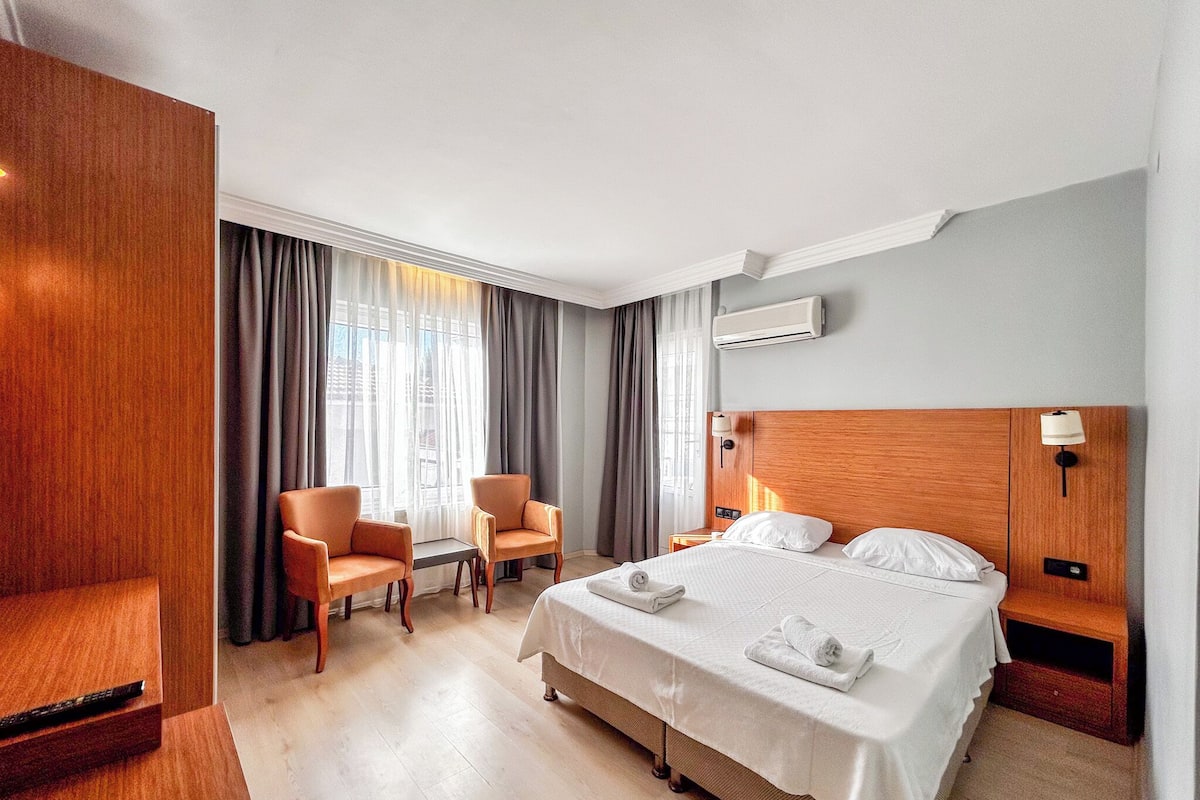 A hotel room with a bed, two chairs, a desk, and a window with curtains.