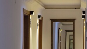 Un pasillo con un espejo que refleja el corredor, suelo alfombrado y lámparas fijadas a la pared.