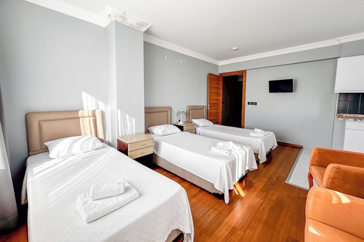 A hotel room with three single beds, a wooden floor, a flat-screen TV, and a small kitchenette.
