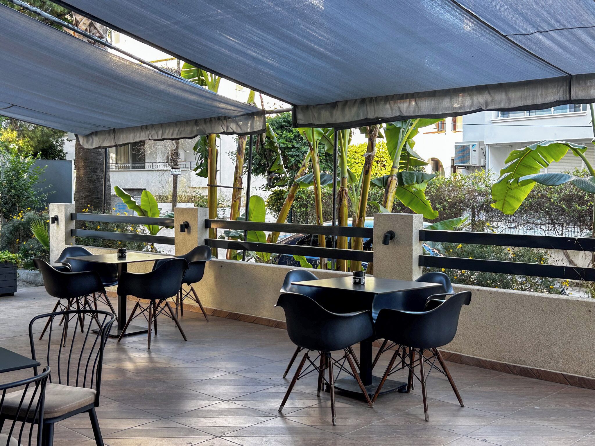 Un patio al aire libre con mesas y sillas, una zona cubierta y vistas a edificios y vegetación.