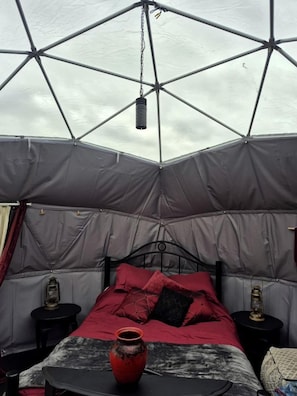 A tent with a bed, two side tables, and a hanging light fixture.