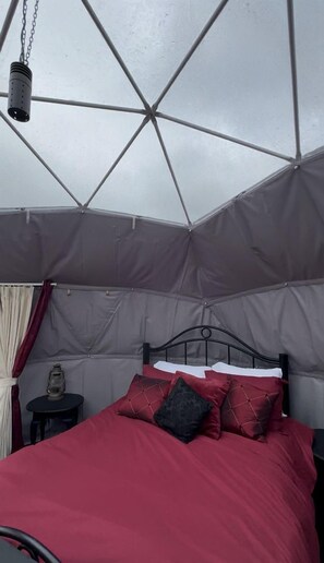 Una tenda-stanza con un letto, un tavolino con una lanterna e una struttura di metallo per il letto.