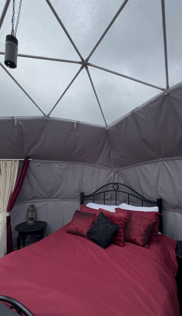 A tent-style room with a bed, a small table with a lantern, and a metal bed frame.