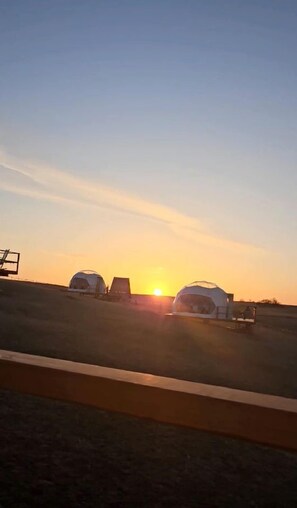 A sunset with two dome-shaped structures in a field.