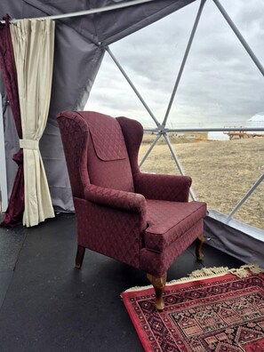 A tent with a red patterned chair, a beige curtain, and a red patterned rug.