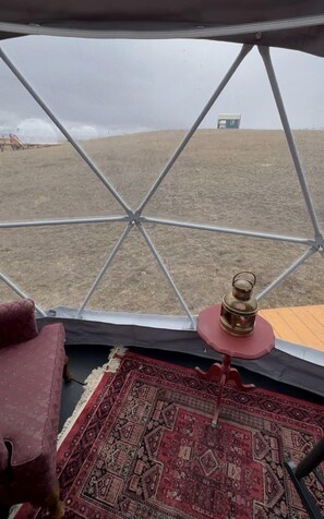 A tent with a view of a field, a lantern, and a patterned rug.