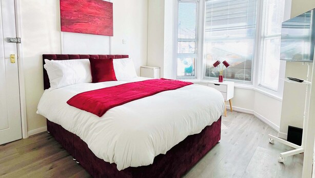 Un dormitorio moderno con una cama grande, ropa de cama blanca, un plaid rojo y un cuadro abstracto rojo en la pared.