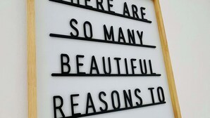 Un cartel enmarcado con el texto 'HAY TAN BELLAS RAZONES PARA SER FELIZ'.
