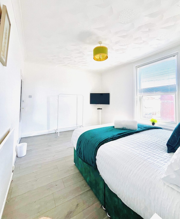 A bedroom with a bed, a TV, a window, and a ceiling light.