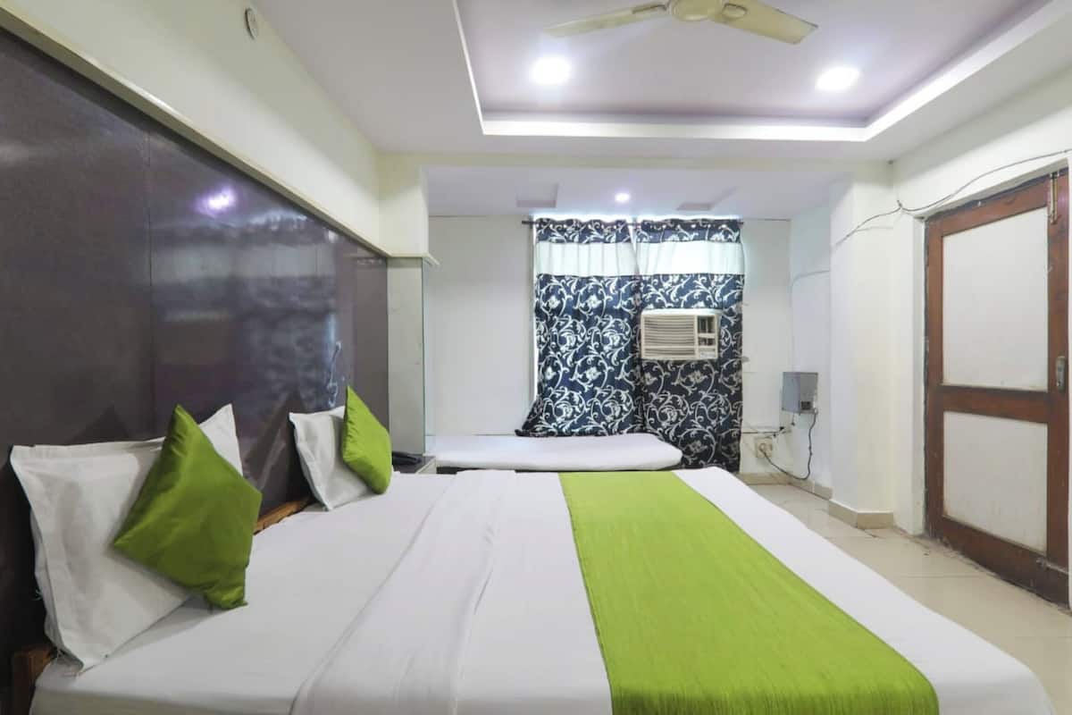 A hotel room with a bed, a small table, a ceiling fan, an air conditioning unit, and a door.