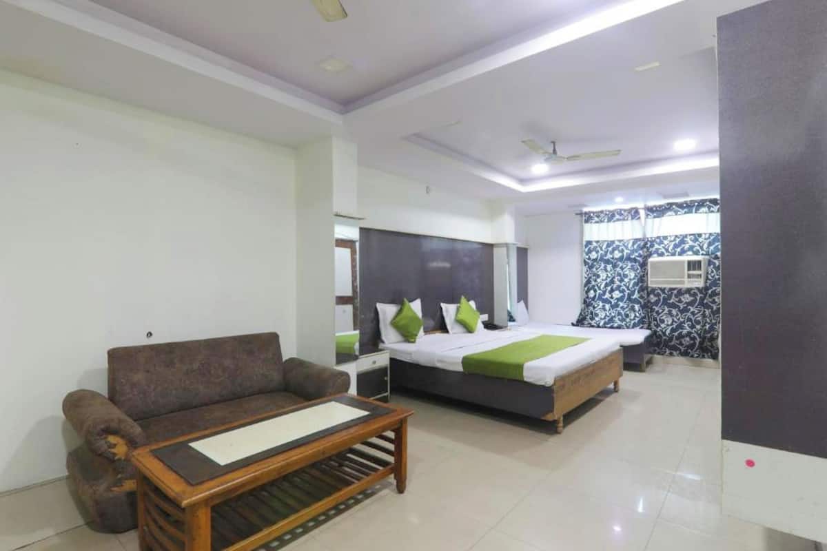 A hotel room with a sofa, a bed with green pillows, a bedside table, and a ceiling fan.