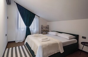 A bedroom with a bed, pillows, a bedside table, a striped rug, and a window with curtains. - Mansarda Old City Avlabari (Tbilisi)