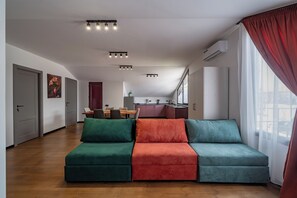 A modern living room with a sofa, dining area, kitchen, and large windows. - Mansarda Old City Avlabari (Tbilisi)