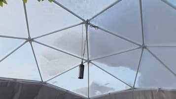 A tent with a bed, a hanging light, and a plant.