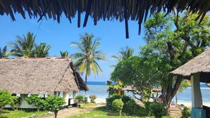 A beachside property with thatched-roof structures, a clear view of the ocean, and lush greenery. - Twiga Lodge Tiwi (Tiwi)