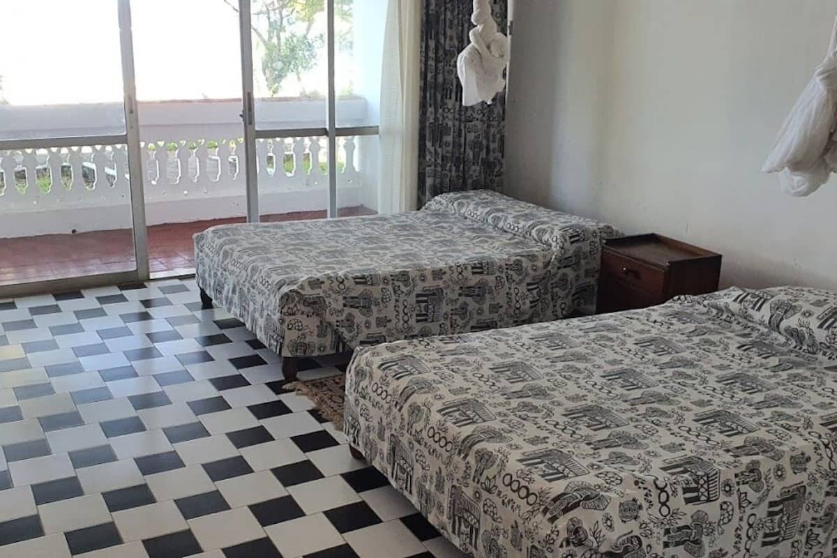 A room with two beds, a checkered floor, a balcony with a view, and a hanging towel.
