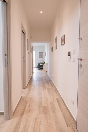 A hallway with a wooden floor, white walls, and framed pictures. There are doors on both sides, and a desk with a chair in the distance. - Panoramic house in the heart of Salento, 20 min from the two seas (Galatina)