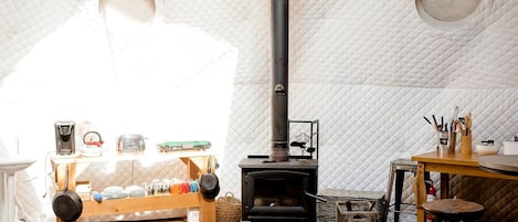 A cozy room with a quilted ceiling, a black wood-burning stove, a wooden table with kitchenware, and a rustic chair.
