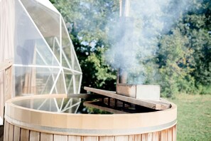 Un bain à remous doté d’un couvercle transparent, de la vapeur s’en échappant, et d’une structure en bois.