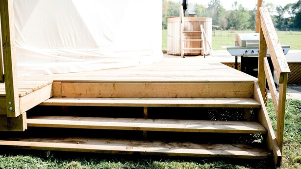 A wooden deck leading to a tent with a grill and a ladder. - Unique Off-Grid Dome Escape with Hot Tub & Forest Views in Ontario, Canada (Marmora)