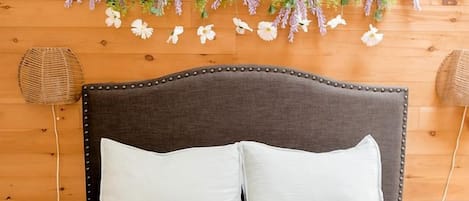 A bed with white bedding, a dark headboard, and a wooden wall with hanging floral decorations.